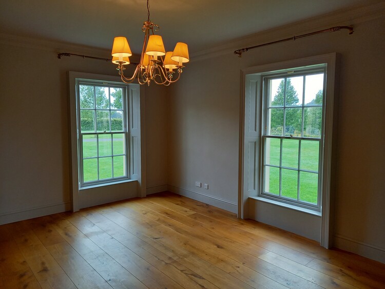 A room with two tall sash windows, wooden flooring and freshly-painted walls.